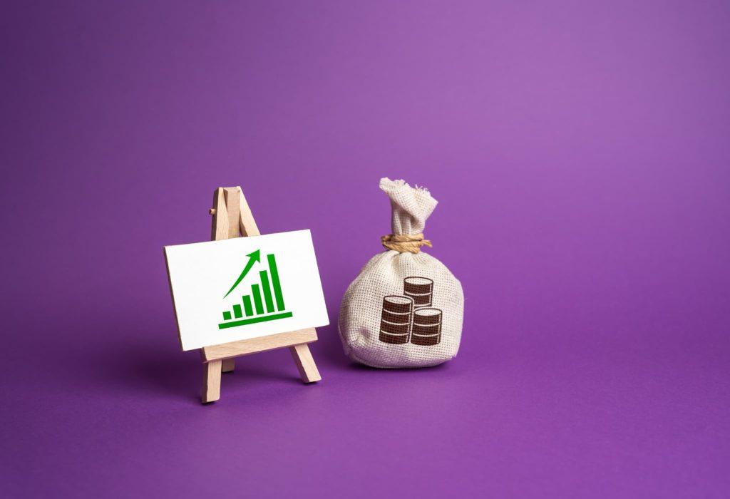 右肩上がりのグラフが描かれたミニイーゼルと硬貨のイラストが描かれた袋。少額のファクタリング活用による売上向上やキャッシュフローの健全化を象徴