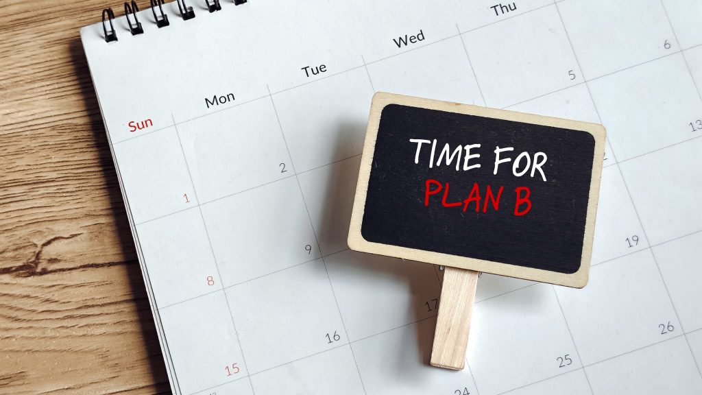 カレンダーの上に置かれた「TIME FOR PLAN B」と書かれた小さな黒板。融資が受けられない場合に備え、個人事業主が運転資金確保の代替案を検討する重要性を表現