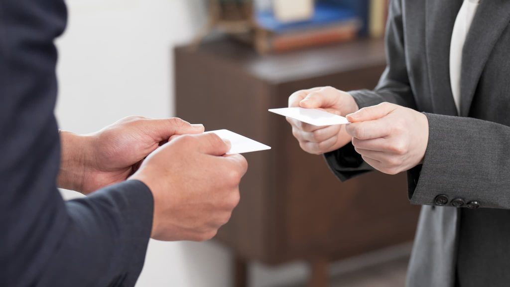 ビジネスシーンで名刺交換を行う二人の手元。個人事業主が新たな取引先を開拓し、事業を継続するための運転資金や融資の必要性をイメージ