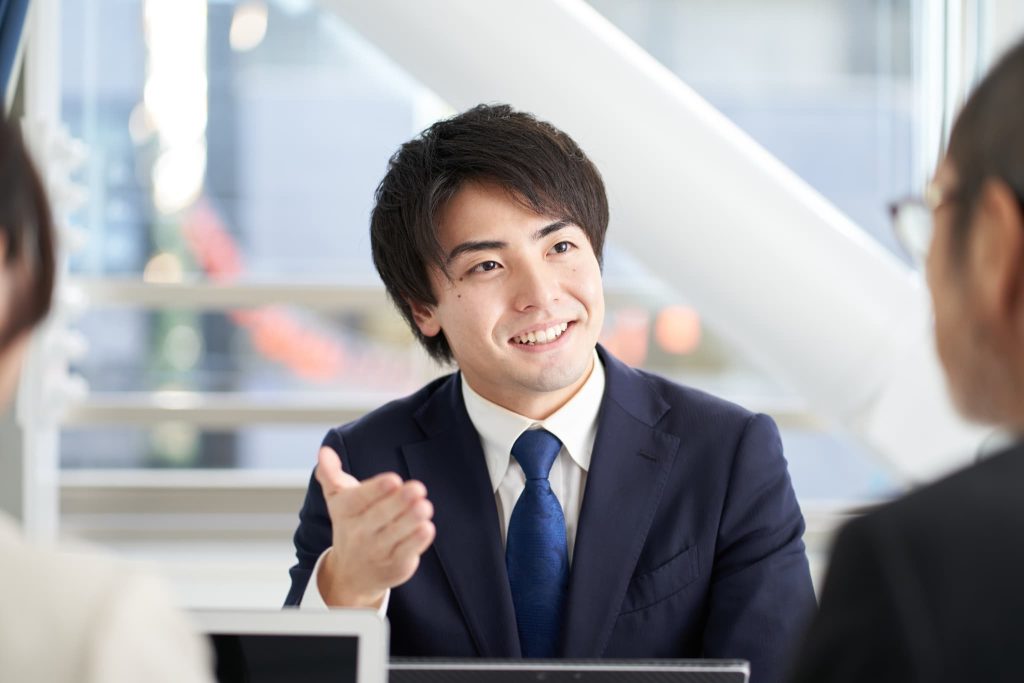 相談相手に対して笑顔で説明を行うスーツ姿の男性。金融機関や専門家から法人ビジネスローンの融資についてアドバイスを受けている前向きなビジネスシーン