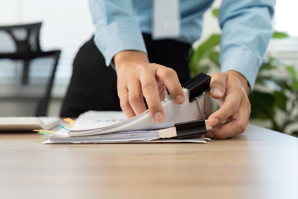 デスクの上で大量の書類ファイルをめくり内容を確認する手元。法人ビジネスローンの審査に向けた決算書や事業計画書の整理作業をイメージ