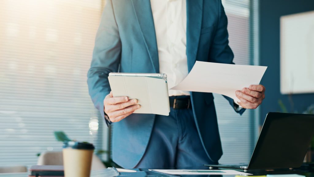 オフィスでタブレットと書類を手に持ち確認を行うビジネスパーソン。法人ビジネスローンの申し込み手続きや必要書類の準備を進めている様子