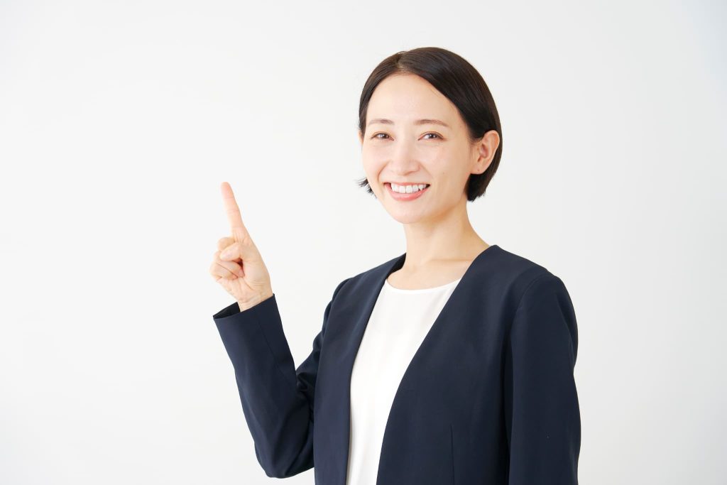 笑顔で人差し指を立ててポイントを指し示す紺色のジャケットを着た女性。おすすめの法人向けビジネスローンや契約の決め手を案内するポーズ