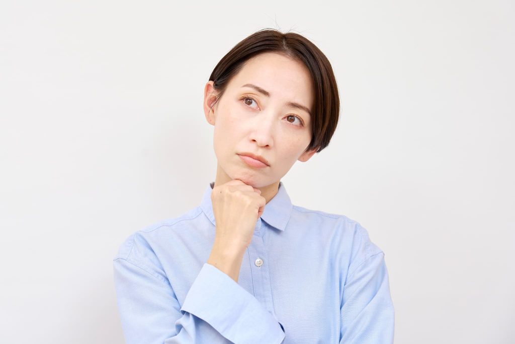 顎に手を当てて悩む表情を浮かべる女性。法人経営者が資金繰りやビジネスローンの活用について検討している不安な心理状況を表現