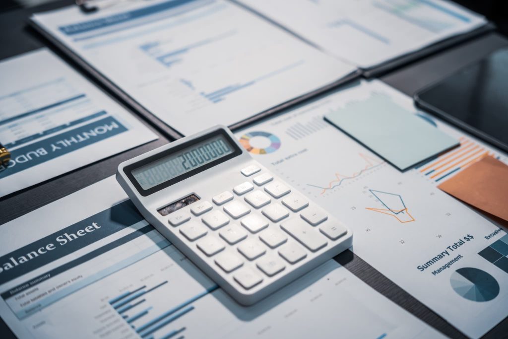 デスクに広げられた貸借対照表（Balance Sheet）などの財務書類と白い電卓。個人事業主が融資審査に向けて現在の運転資金や収支状況を計算している様子