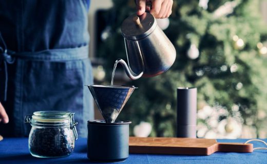 カフェの起業・開業手順を解説するイメージ写真。青いエプロンをつけたスタッフが、ポットからお湯を注ぎ、ハンドドリップでコーヒーを抽出している