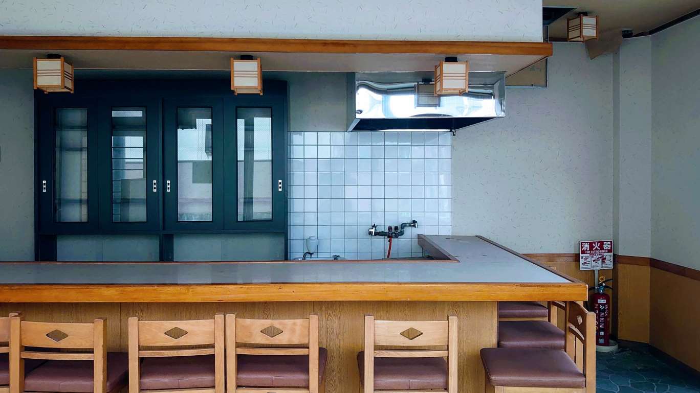 写真:居抜き物件のイメージ。カウンターや椅子、奥の厨房設備など、前のテナントが使用していた内装や造作物がそのまま残っている