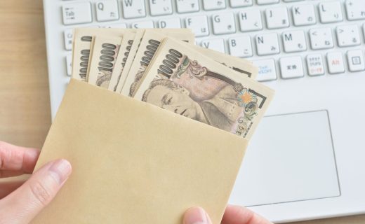 個人事業主が補助金として受け取る現金をイメージした写真。茶封筒に複数の1万円札が入っており、背景には作業中のノートパソコンが見えている