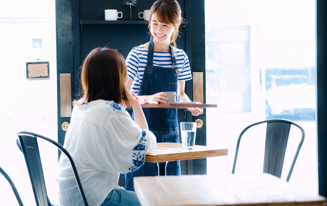 飲食店のオペレーション改善について解説する記事のメイン画像。笑顔の女性スタッフが接客している様子