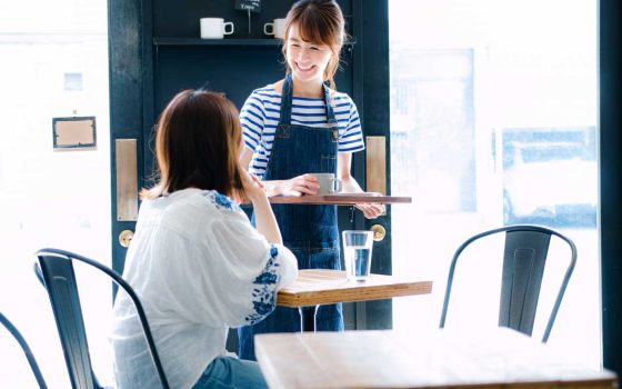 飲食店のオペレーション改善について解説する記事のメイン画像。笑顔の女性スタッフが接客している様子