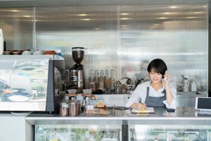 自営業の始め方を解説する記事のメイン画像。おしゃれなカフェのカウンターで、オーナーである女性が電話で予約を受け付けている様子