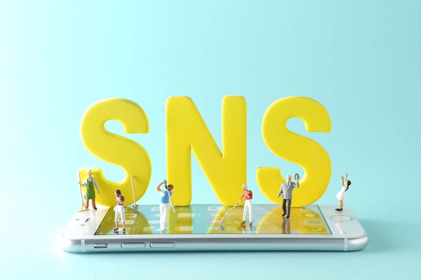 SNS広告とは何かを解説する記事のメイン画像。スマートフォンの上に置かれた「SNS」の文字の周りにミニチュアの人々が立っている
