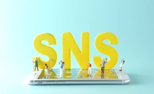 SNS広告とは何かを解説する記事のメイン画像。スマートフォンの上に置かれた「SNS」の文字の周りにミニチュアの人々が立っている