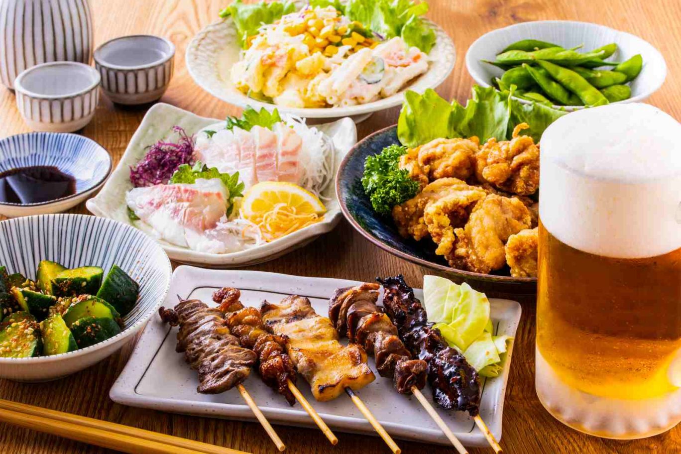 飲食店の原価率の計算方法を解説する記事のメイン画像。テーブルに並んだ焼き鳥や唐揚げ、刺身などの料理で、メニュー全体の原価の重要性を表現
