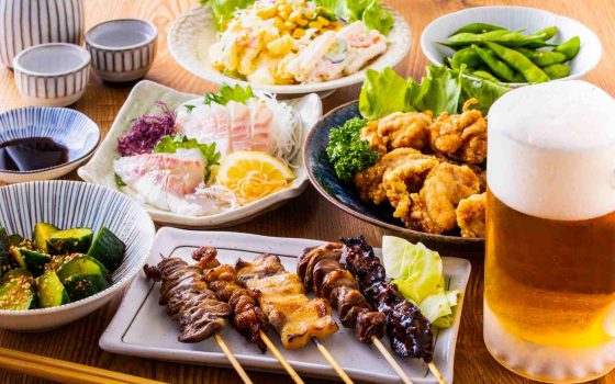 飲食店の原価率の計算方法を解説する記事のメイン画像。テーブルに並んだ焼き鳥や唐揚げ、刺身などの料理で、メニュー全体の原価の重要性を表現