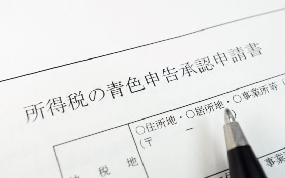 青色申告の手続きをイメージした写真。「所得税の青色申告承認申請書」の用紙の上に、記入しようとするペンが置かれている