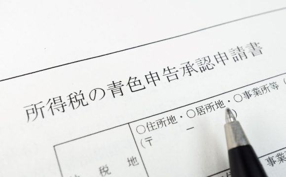 青色申告の手続きをイメージした写真。「所得税の青色申告承認申請書」の用紙の上に、記入しようとするペンが置かれている