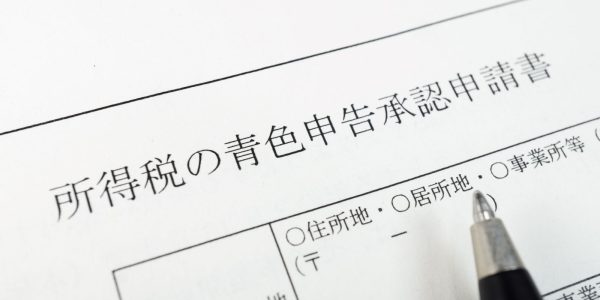 青色申告の手続きをイメージした写真。「所得税の青色申告承認申請書」の用紙の上に、記入しようとするペンが置かれている