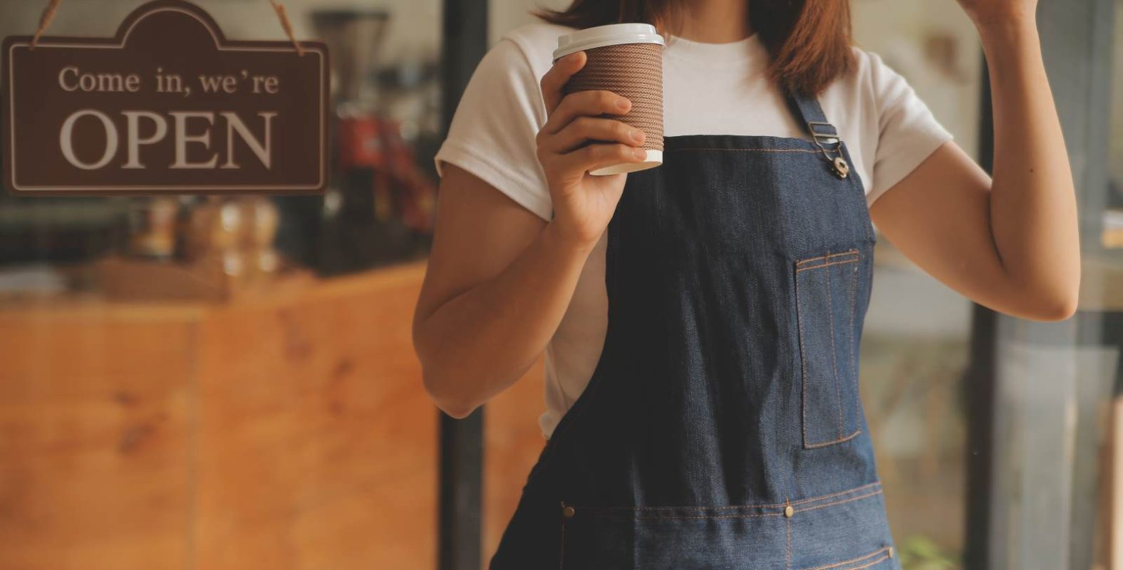店舗開業をイメージした写真。エプロンをつけた女性が、「OPEN」と書かれた看板が掛かった店舗入口前で、コーヒーカップを片手にガッツポーズをしている