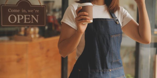 店舗開業をイメージした写真。エプロンをつけた女性が、「OPEN」と書かれた看板が掛かった店舗入口前で、コーヒーカップを片手にガッツポーズをしている