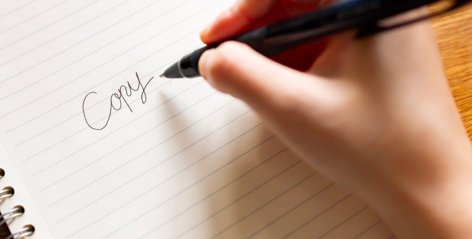 キャッチコピー制作をイメージした写真。白いノートに黒いペンで、「Copy」という文字を手書きしている様子
