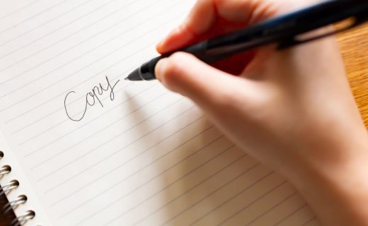 キャッチコピー制作をイメージした写真。白いノートに黒いペンで、「Copy」という文字を手書きしている様子