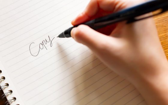 キャッチコピー制作をイメージした写真。白いノートに黒いペンで、「Copy」という文字を手書きしている様子