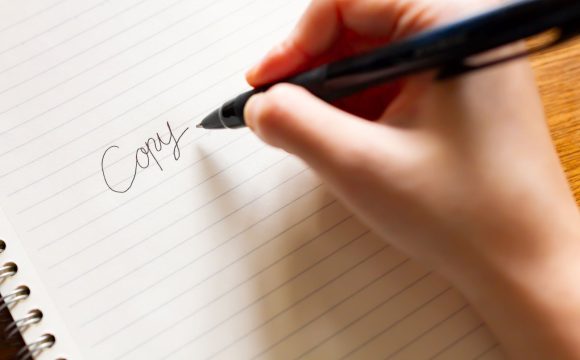 キャッチコピー制作をイメージした写真。白いノートに黒いペンで、「Copy」という文字を手書きしている様子