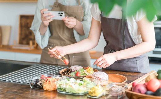 飲食店のメニュー開発の手順を解説する記事のメイン画像。エプロン姿のスタッフが、試作した料理の盛り付けを調整し、スマートフォンで記録・撮影している様子を表現