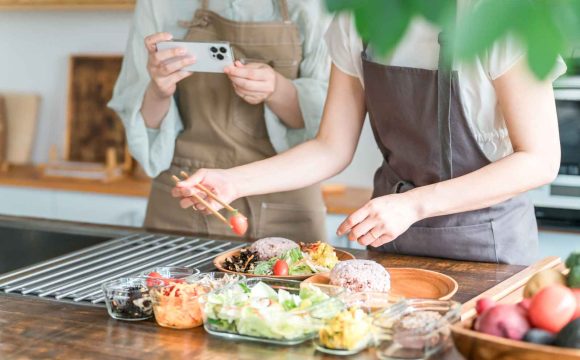 飲食店のメニュー開発の手順を解説する記事のメイン画像。エプロン姿のスタッフが、試作した料理の盛り付けを調整し、スマートフォンで記録・撮影している様子を表現