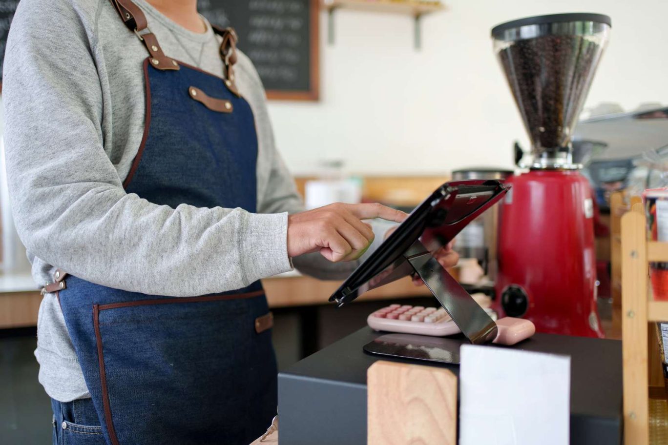 記事のメイン画像：飲食店（カフェ）のカウンターでエプロン姿のスタッフがタブレット型POSレジを操作し売上管理をしている様子